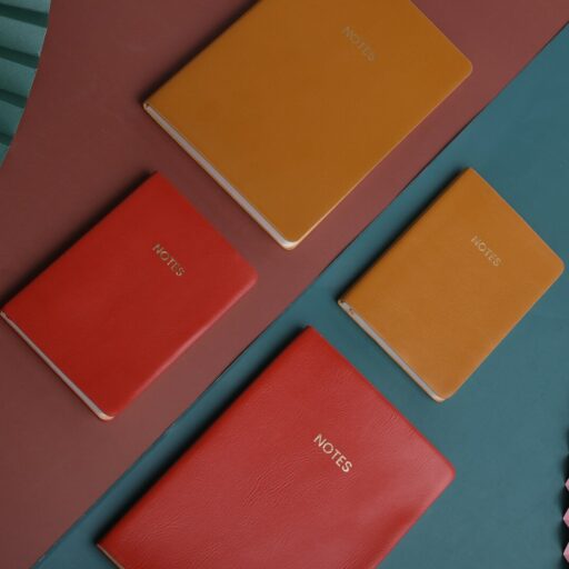 three different colored notebooks next to a pink fan